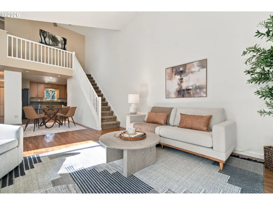 Staged open living room with a cream sofa, round coffee table and a staircase leading to a loft