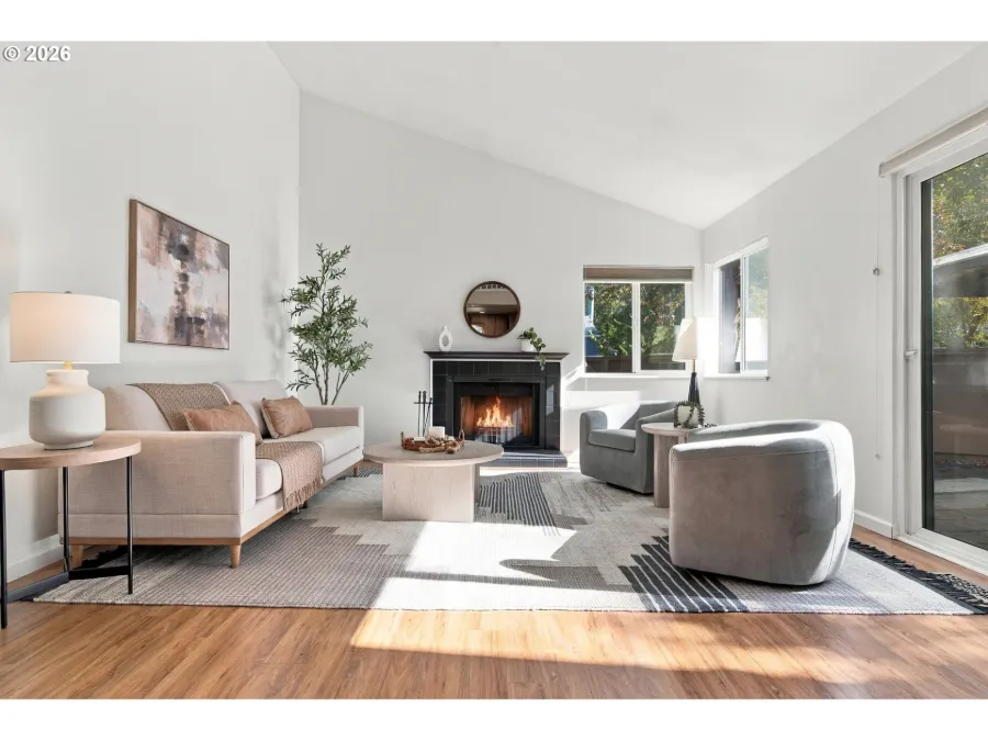 Staged living room with a blush sofa, swivel chair and a lit fireplace under a vaulted ceiling