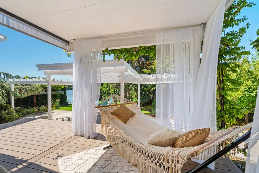 Staged covered patio with a woven hammock, cushions and sheer curtains overlooking a garden