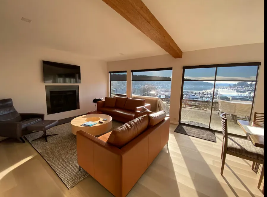 Sunlit rental living room with a cognac leather sofa, round coffee table and sliding doors to a waterfront deck